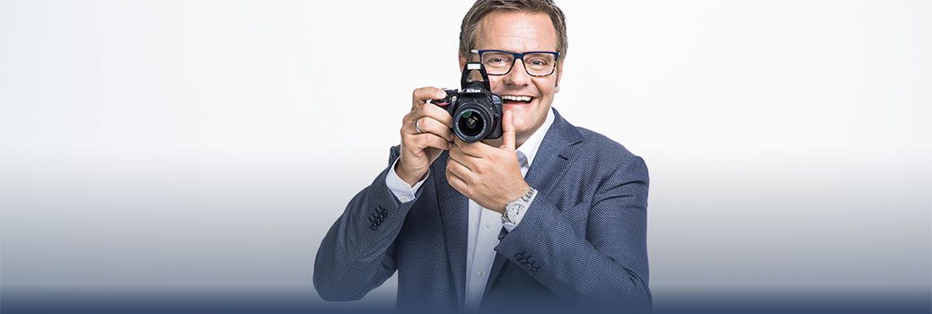 Unternehmer Robert Hartlauer lacht und fotografiert in die Kamera